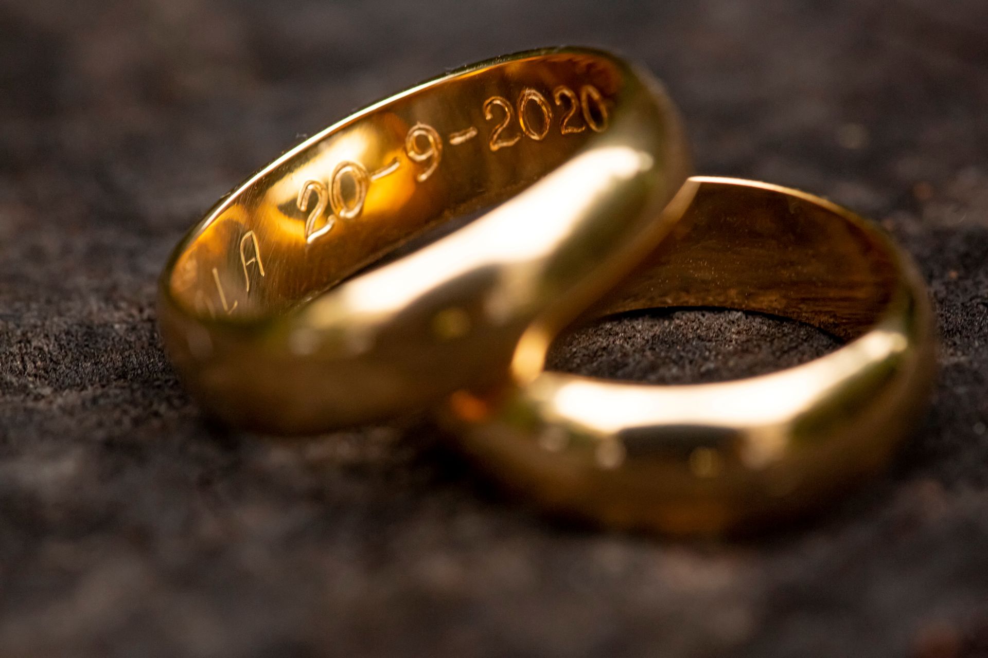 Zwei goldene Trauringe mit eingraviertem Datum liegen auf dunklem Untergrund – Fokus auf persoenlicher Gravur
